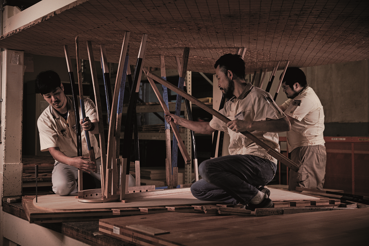 Piano artisans crafting a wooden grand piano rim in a workshop setting.
