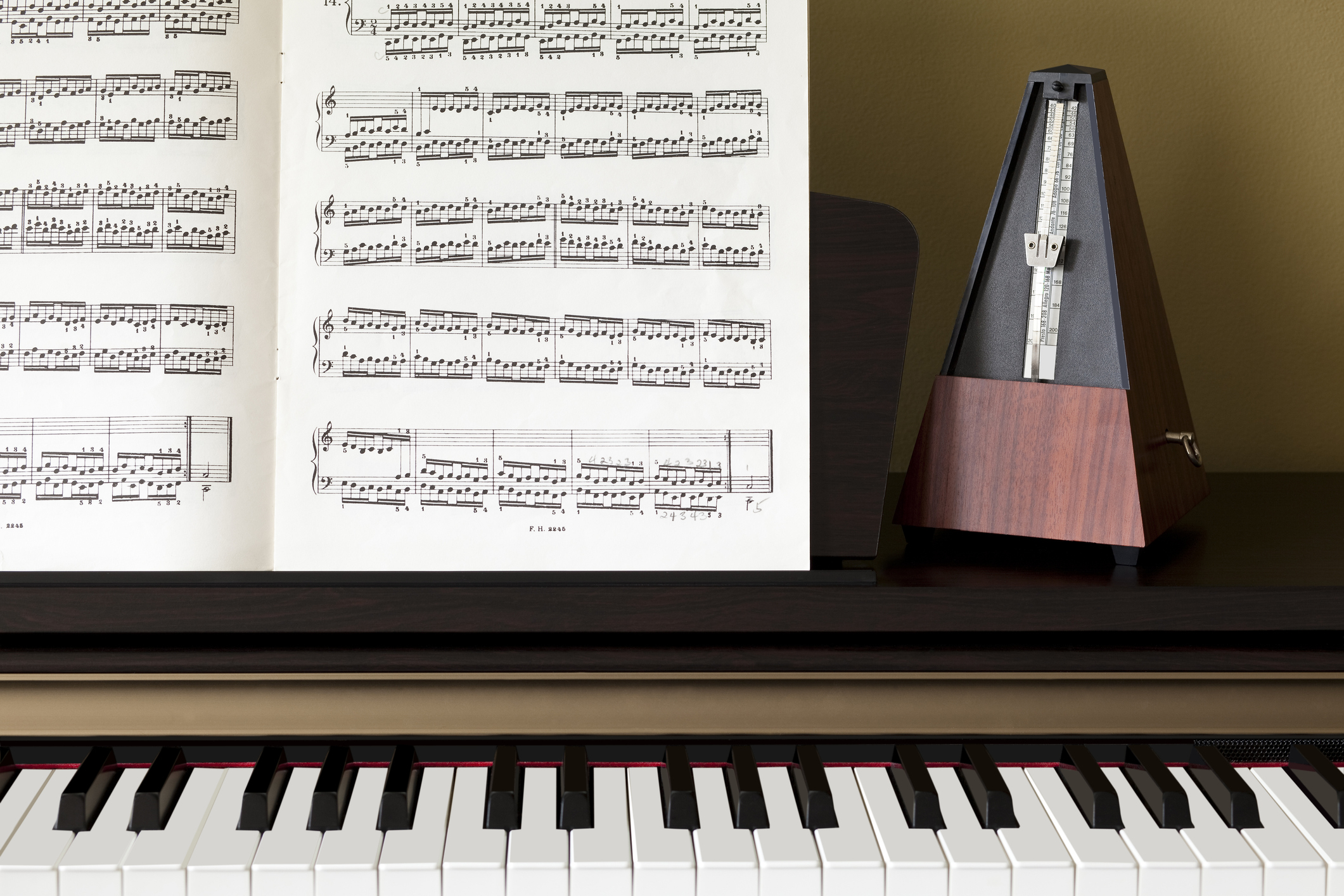 Piano keyboard close-up with sheet music and wooden metronome on the music stand.