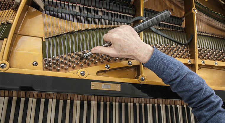 hand and tools of tuner working on grand piano Adjusting piano strings with tuning lever inside a grand piano.