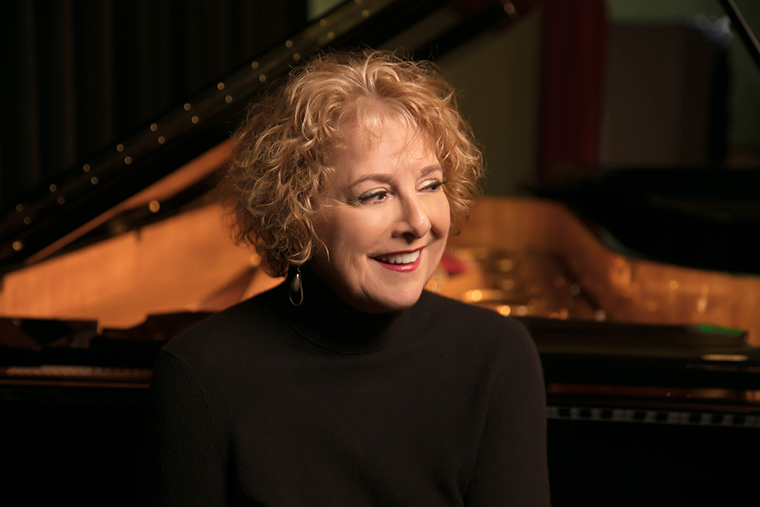 Woman smiling in front of grand piano in a showroom.