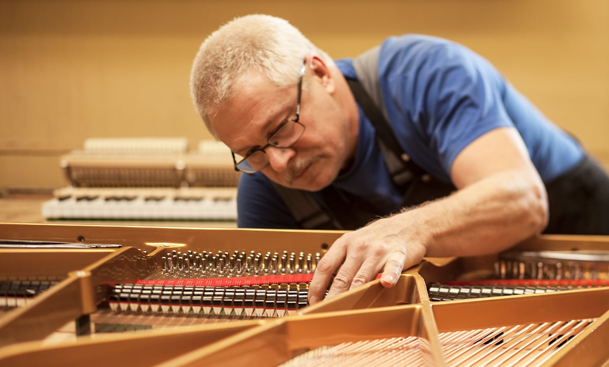 Estonia Piano Maker Piano technician tuning strings inside grand piano in workshop setting.