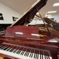 Mahogany grand piano with open lid, showcased in a piano showroom, Yamaha logo visible in the background.